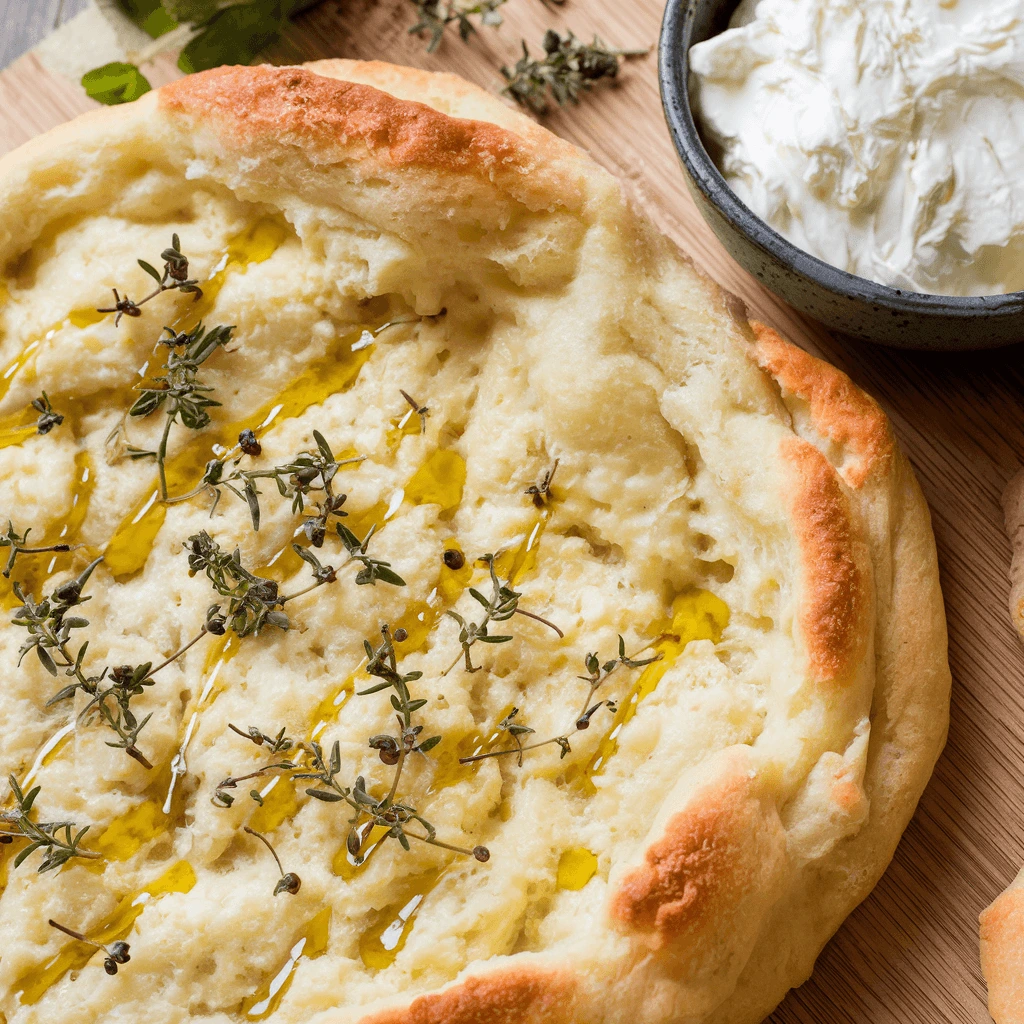 A stack of warm, soft cottage cheese flatbread ready to serve with hummus and tzatziki.
